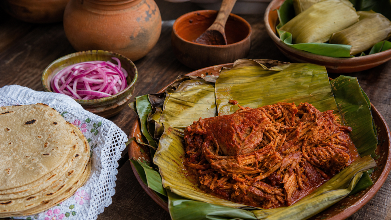 Cochinita pibil yucateca envuelta en hoja de plátano, con cebolla morada encurtida y tortillas