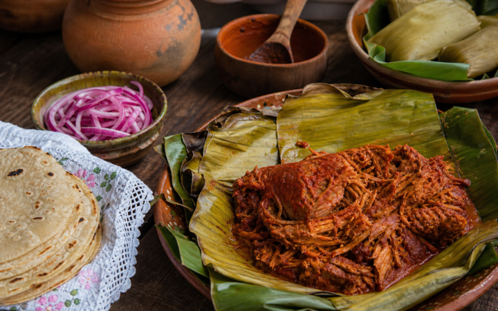 Cochinita pibil yucateca envuelta en hoja de plátano, con cebolla morada encurtida y tortillas