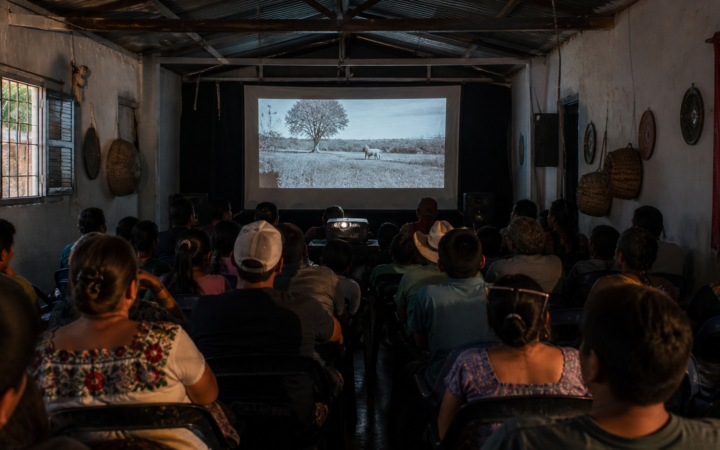 Sala de cine comunitaria con proyector encendido y butacas listas para una función.