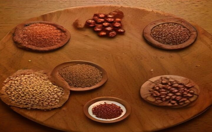 Ilustración vista desde arriba de una tabla redonda de madera con cuencos de barro llenos de semillas, especias molidas, granos de cacao y trozos de chile seco, algunos de los ingredientes del mole poblano