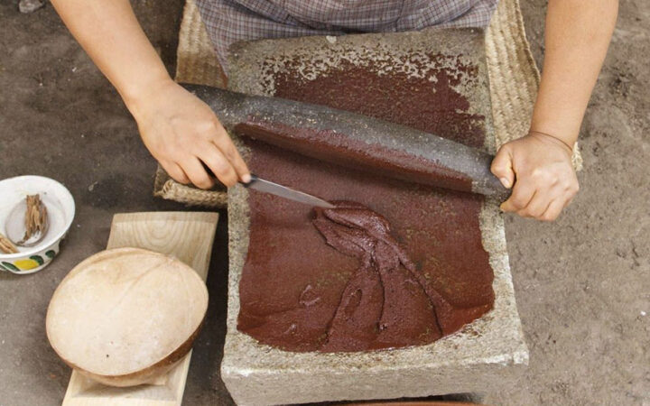 Manos que muelen una preparación de cacao sobre un metate.