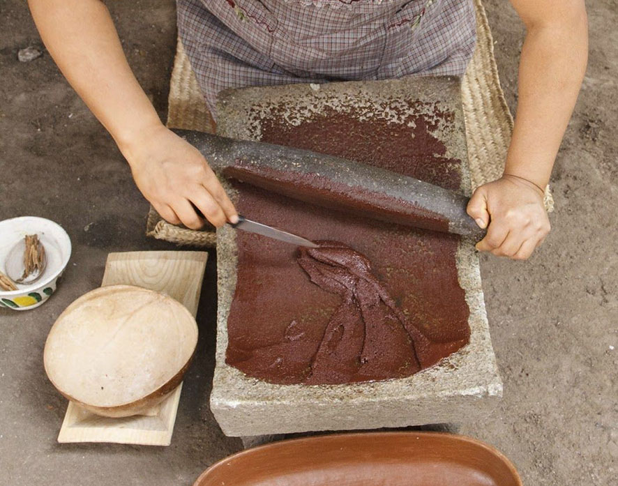 Manos que muelen una preparación de cacao sobre un metate.